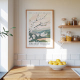 a kitchen scene with a framed poster of a blooming almond tree on the wall, a wooden counter with a bowl of lemons, and shelves displaying various jars and containers.