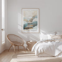 A bedroom with a bed, a woven chair, and a framed poster of a staircase on the wall.