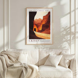 a framed poster of a desert landscape with mountains in the background, hanging on a white wall above a white couch with a blanket draped over it.