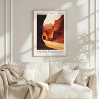 a framed poster of a desert landscape with mountains in the background, hanging on a white wall above a white couch with a blanket draped over it.