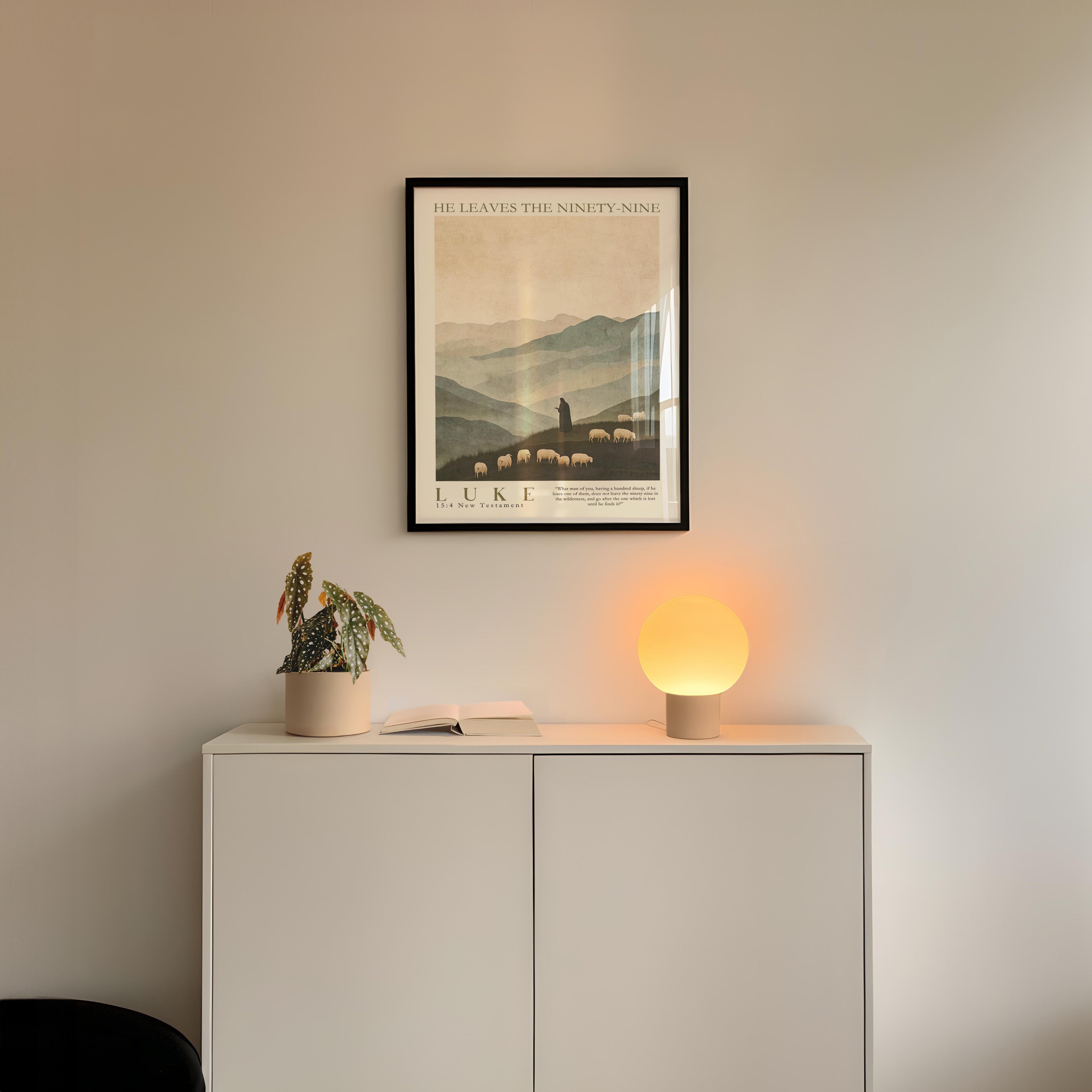 a minimalist interior design with a framed poster of a mountain landscape, a potted plant, and a small lamp on a white cabinet.