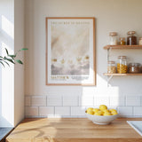 A framed poster of a cloudy sky with crowns hangs on a white wall above a wooden countertop with a bowl of lemons.