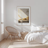 A bedroom with a bed, a woven chair, and a framed poster of a still life of bread and fruit on the wall.