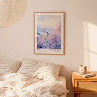 a bedroom scene with a framed poster of a woman in a field of flowers hanging on the wall above a bed with striped pillows.