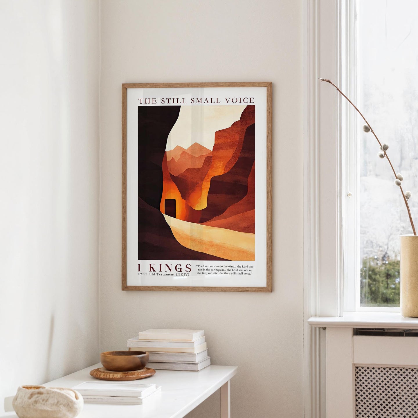 a framed poster of a desert landscape with mountains, hanging on a wall in a room with a white table and a window.