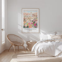 A bedroom with a large bed, a woven chair, and a framed poster of a cityscape with flowers hanging on the wall.