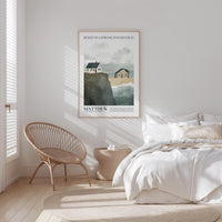 a serene bedroom scene with a bed, a woven chair, and a framed poster of a coastal landscape.