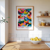 a kitchen scene with a framed poster of colorful birds hanging on the wall above a wooden countertop. On the countertop, there is a bowl of lemons and a plant.