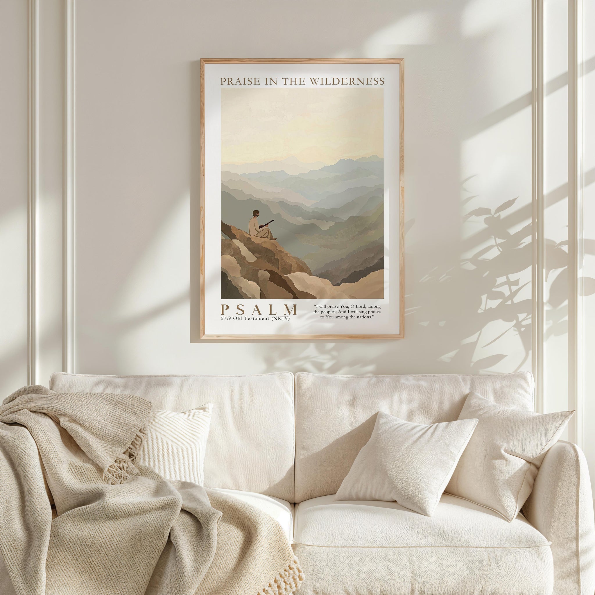 a framed poster of a person sitting on a mountain, with a serene landscape in the background. The poster is titled "PRAISE IN THE WILDERNESS" and includes a Bible verse from the book of Psalms. The poster is hung on a white wall above a white couch, which has a blanket draped over it.