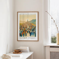 a framed poster of a large crowd of people, with the text "JESUS fed the five thousand" and "MATTHEW 1419 New Testament" below it. The poster is hanging on a wall, and there is a small table with a stack of books and a vase on it.