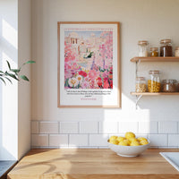 A framed poster of a pink and white floral scene hangs on a white wall above a wooden countertop with a bowl of lemons.