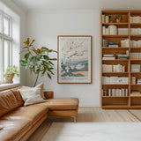 a cozy living room with a large bookshelf filled with books, a comfortable leather sofa, and a framed poster of a cherry blossom tree on the wall.