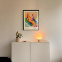 a white cabinet with a plant and a lamp on top, and a framed poster hanging on the wall above the cabinet.