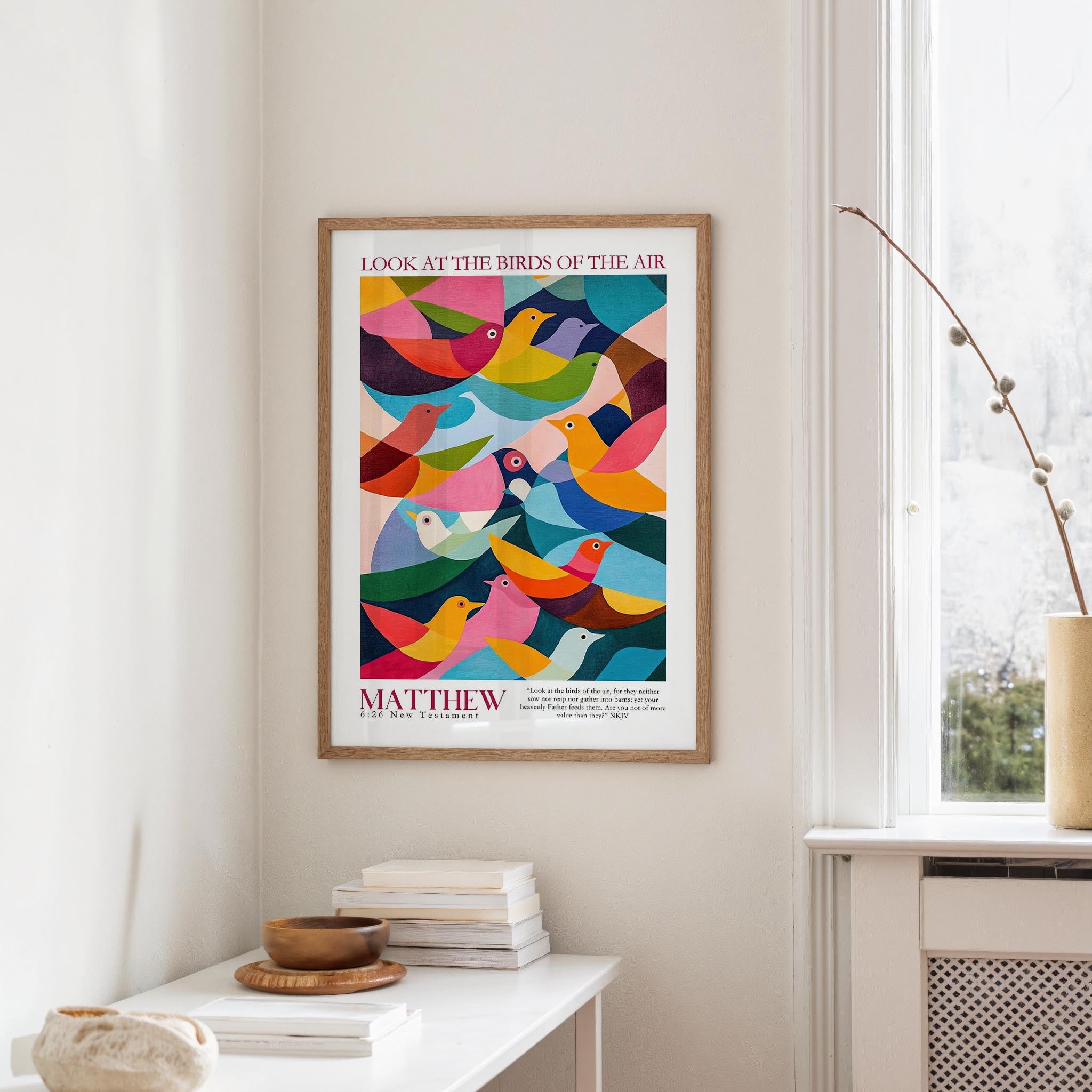 a colorful poster of birds hanging on a wall, with a stack of books and a vase on a table below it.