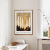 a framed poster of a group of people in a church, hanging on a wall in a room with a window and a table with books and a bowl on it.