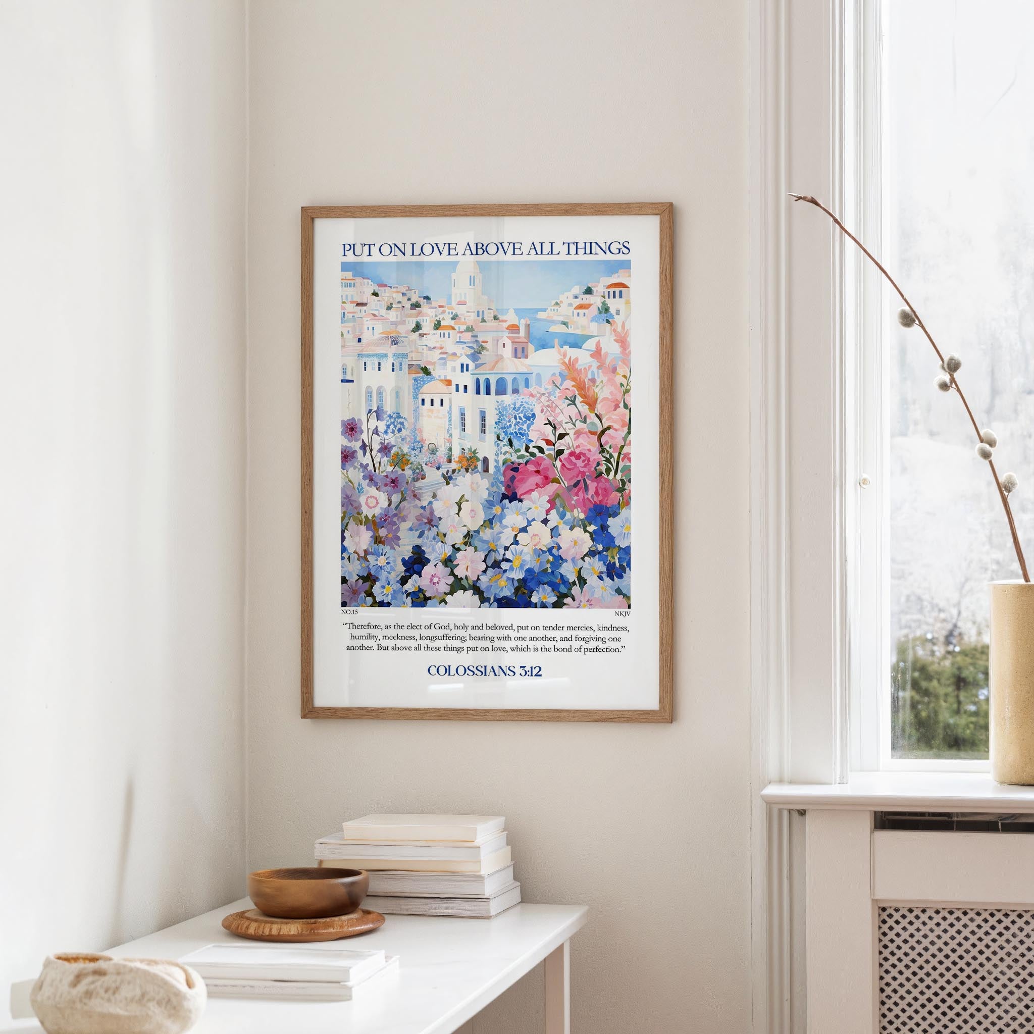 a framed poster of a colorful floral scene hanging on a wall, with a white table and a vase of flowers in the foreground.