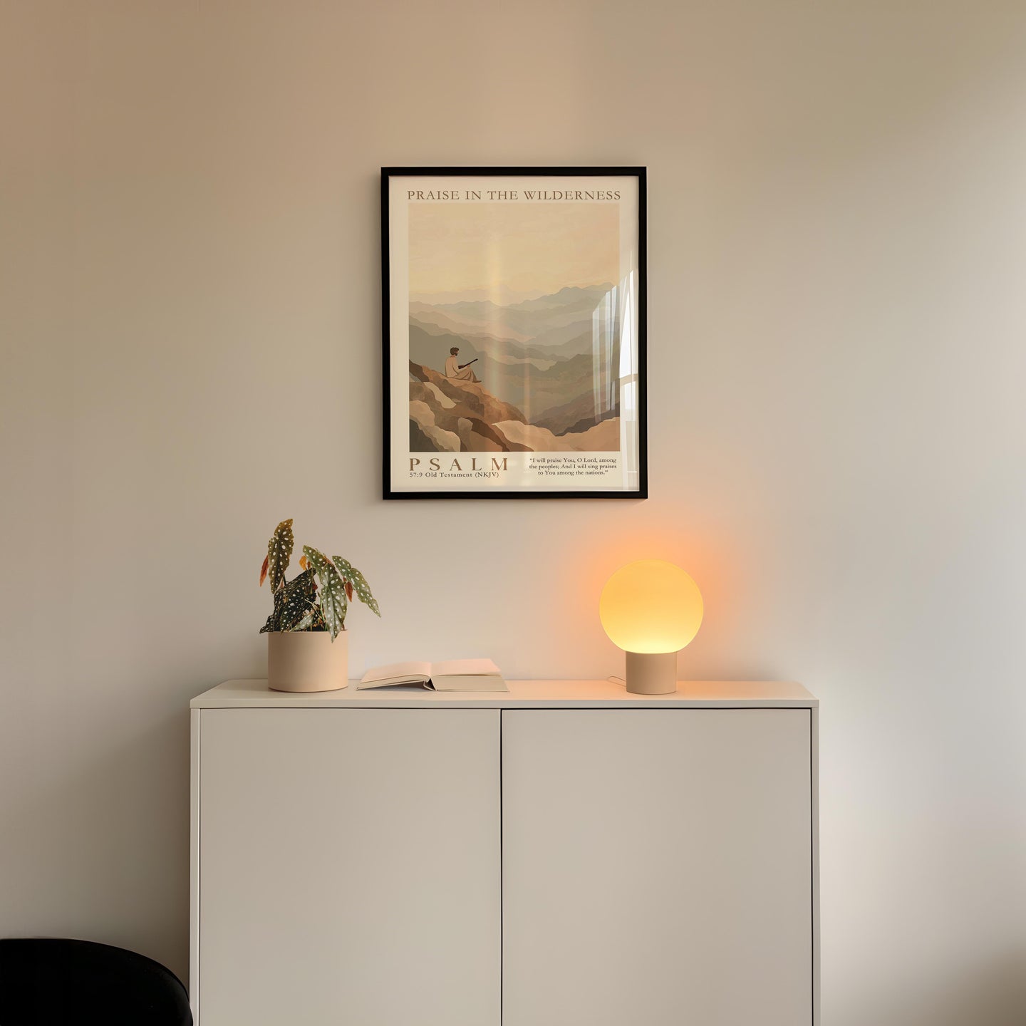 a minimalist interior design with a framed poster of a mountain landscape above a white cabinet with a plant and a lamp on top.