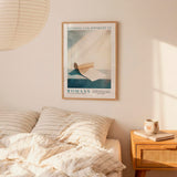 a bedroom setting with a framed poster of a book and a wooden nightstand with a coffee cup and a book.
