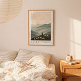 a bedroom scene with a framed poster of a mountain landscape hanging on the wall above a bed with striped bedding.