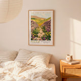 a bedroom scene with a framed poster of a countryside landscape hanging on the wall above a bed with striped pillows.