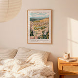 a bedroom scene with a framed poster of a pastoral landscape hanging on the wall above a bed with striped bedding.