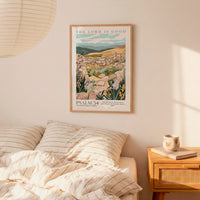 a bedroom scene with a framed poster of a pastoral landscape hanging on the wall above a bed with striped bedding.