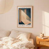 a bedroom scene with a framed poster of a book titled "The Book of Life" hanging on the wall above a bed with striped bedding.