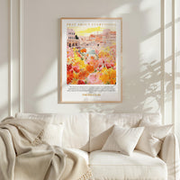a framed poster of a colorful floral scene hanging on a wall above a white couch with pillows.