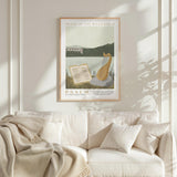 a framed poster of a harp and an open book, hanging on a white wall above a white couch with a blanket draped over it.