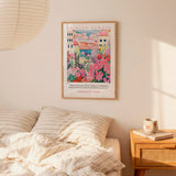 a bedroom scene with a framed poster of a colorful illustration of a cityscape hanging on the wall above a bed with striped pillows.