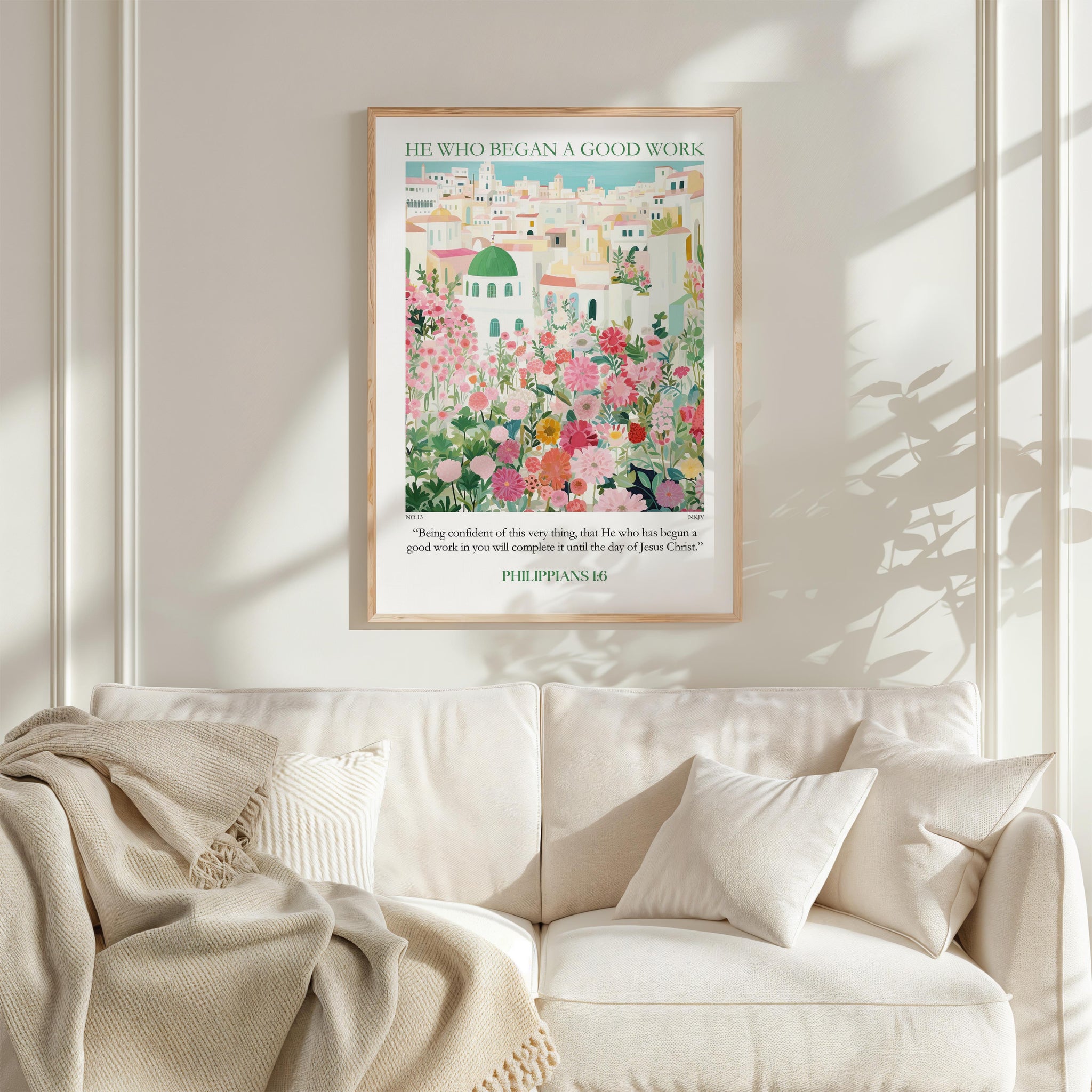 a framed poster of a colorful illustration of a cityscape, hanging on a wall above a white couch with pillows.