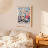 a bedroom scene with a framed poster of a colorful floral landscape hanging on the wall above a bed with striped pillows.