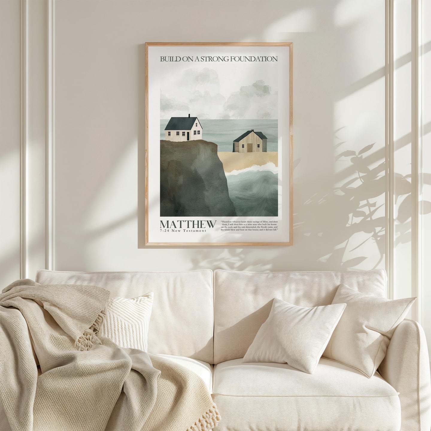 a framed poster of a coastal scene with houses and cliffs, hanging on a wall above a white couch with a blanket draped over it.