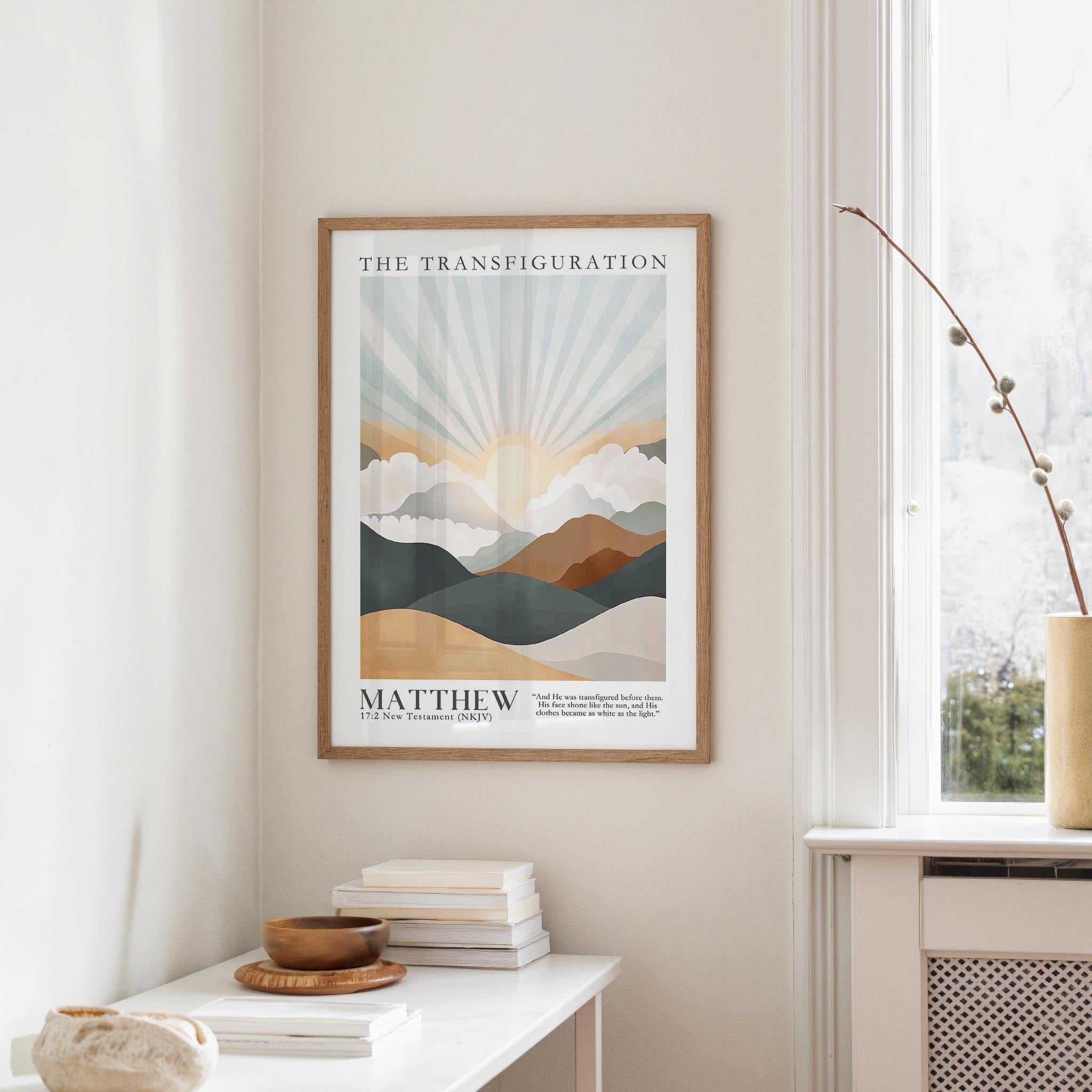 a framed poster of a mountain landscape with a sunburst design, hanging on a wall above a white table with a stack of books and a small vase.