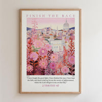 The image is a framed poster with a cityscape and pink flowers as the main elements. The poster features a quote from the Bible, specifically 2 Timothy 4:7, which reads, "I have fought the good fight. I have finished the race. I have kept the faith, and there is laid up for me the crown ofrighteousness, which the Lord will give to one on that Day."