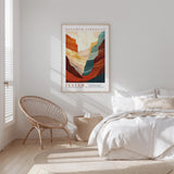 a bedroom with a bed, a woven chair, and a framed poster of a mountain landscape.