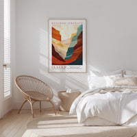 a bedroom with a bed, a woven chair, and a framed poster of a mountain landscape.