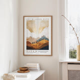 a framed poster of a landscape with mountains and clouds hanging on a wall in a room.
