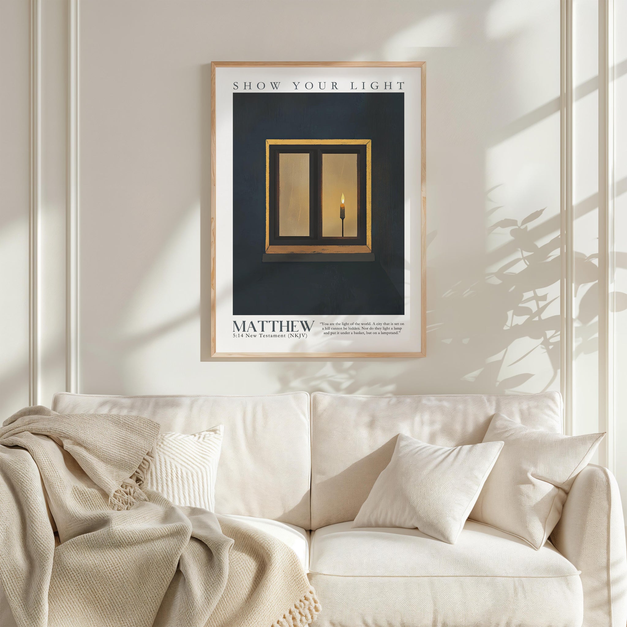 a framed poster of a candle in a window, hanging on a white wall above a white couch with a blanket draped over it.