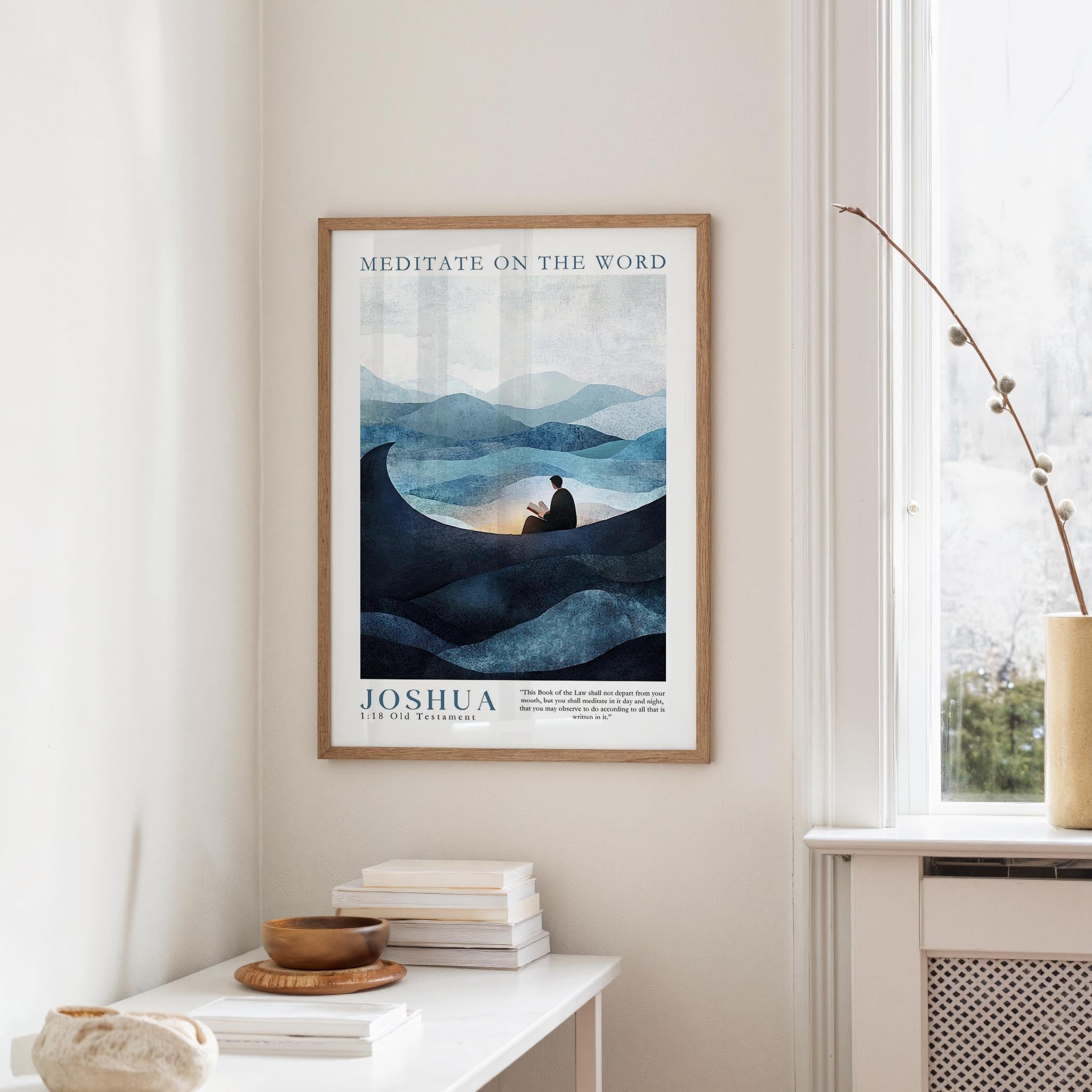 a framed poster of a person meditating in a serene landscape, with mountains and a body of water in the background. The poster is hung on a wall above a white table, which has a stack of books and a small vase on it.