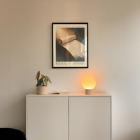 a white cabinet with a plant and a lamp on top, and a framed poster of a book above it.