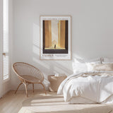 a serene bedroom scene with a bed, a woven chair, and a framed poster of a building.
