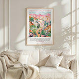 a poster of a desert landscape with buildings and cacti hanging on a wall above a white couch with pillows.