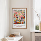 a framed poster of a colorful floral design hanging on a wall, with a white radiator and a stack of books on a table below it.