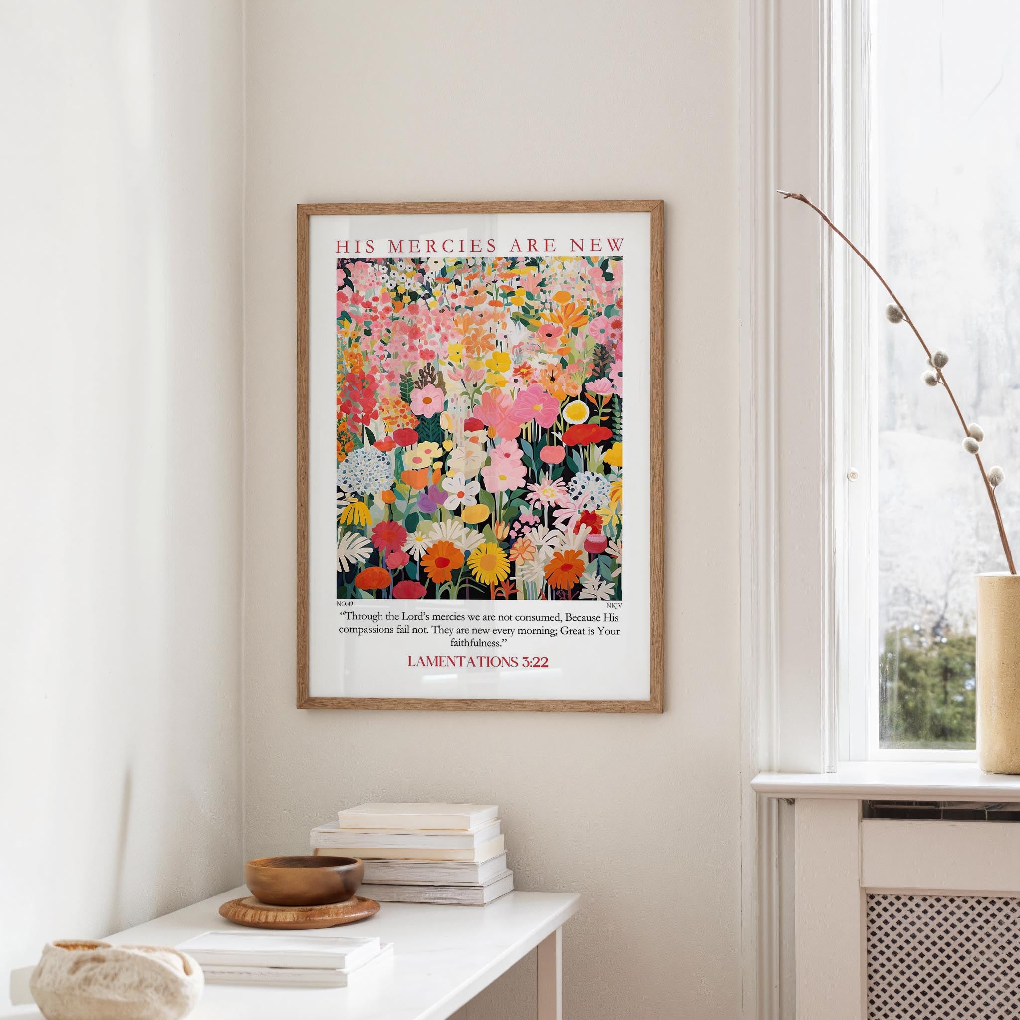 a framed poster of a colorful floral design hanging on a wall, with a white radiator and a stack of books on a table below it.