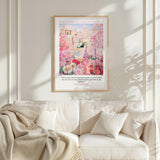 A framed poster of a pink and white floral scene hangs on a white wall above a white couch with a blanket draped over it.