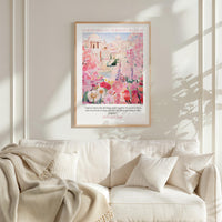 A framed poster of a pink and white floral scene hangs on a white wall above a white couch with a blanket draped over it.