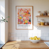 A framed poster of a colorful floral design hangs on a wall above a wooden countertop with a bowl of lemons.