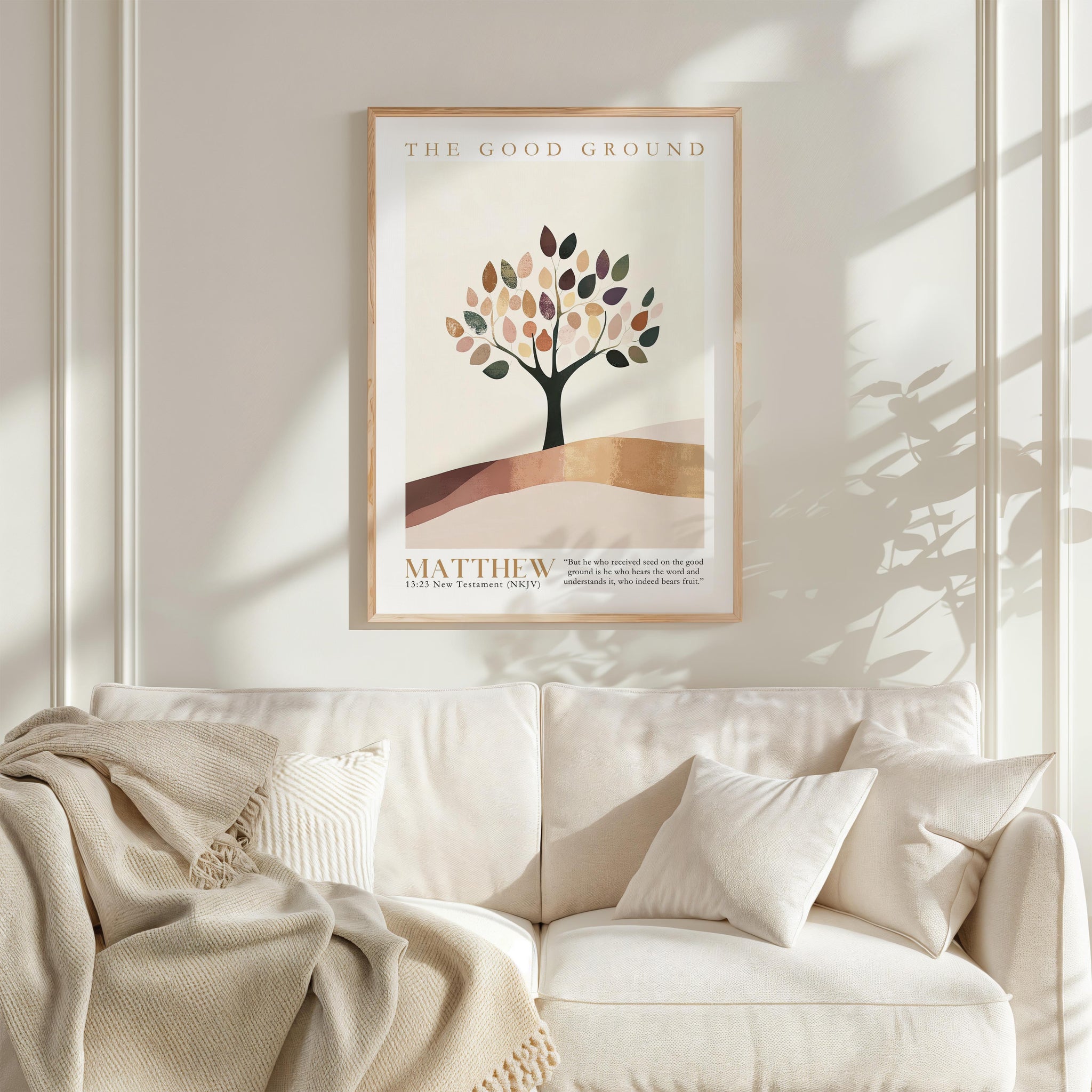 a framed poster of a tree with a text overlay, hanging on a wall above a white couch with a blanket draped over it.