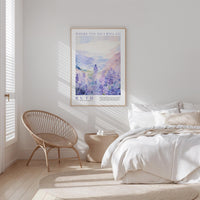 a serene bedroom scene with a large poster of a landscape hanging on the wall, a woven chair, and a neatly made bed with white linens.
